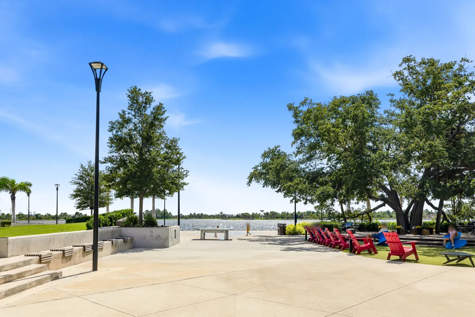Open lakefront plaza with red Adirondack chairs, shade trees and the lake beyond in Wellen Park